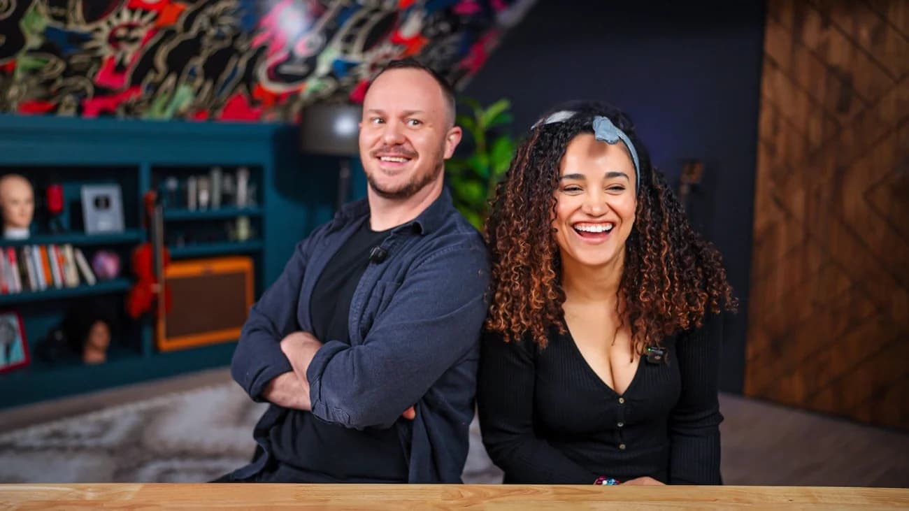 Veronica laughing at their studio desk, with Stephen standing beside her